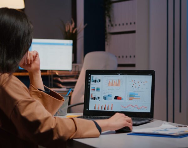Overworked businesswoman typing financial statistics on laptop sitting at desk Overworked businesswoman typing financial statistics on laptop sitting at desk table in startup company office late at night. Workaholic entrepreneur planning economic project before company deadline