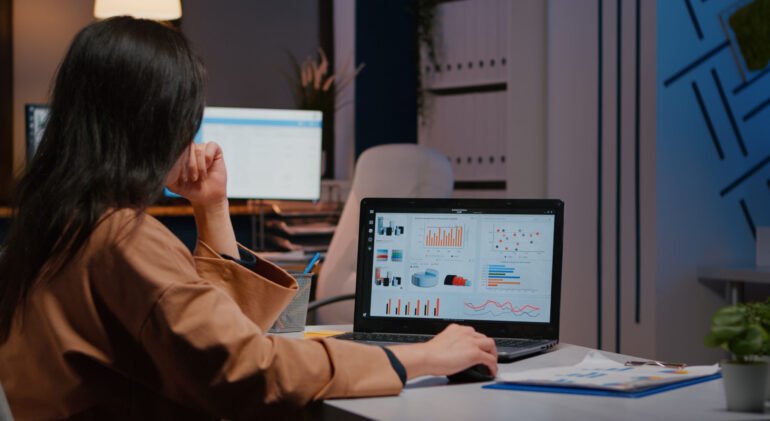 Overworked businesswoman typing financial statistics on laptop sitting at desk Overworked businesswoman typing financial statistics on laptop sitting at desk table in startup company office late at night. Workaholic entrepreneur planning economic project before company deadline