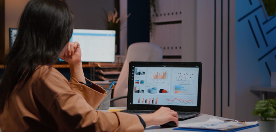 Overworked businesswoman typing financial statistics on laptop sitting at desk Overworked businesswoman typing financial statistics on laptop sitting at desk table in startup company office late at night. Workaholic entrepreneur planning economic project before company deadline